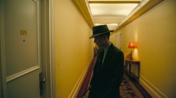 Movie still from “Oppenheimer” (2023), directed by Christopher Nolan – A man in a suit and a hat standing in the hallway of a hotel room; Medium shot, Low angle