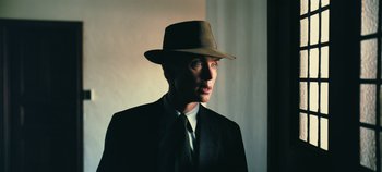 Movie still from “Oppenheimer” (2023), directed by Christopher Nolan – A man wearing a suit and hat in the dark; Close Up shot, High angle