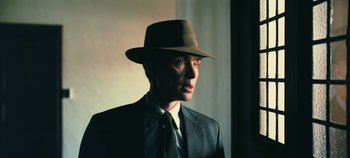 Movie still from “Oppenheimer” (2023), directed by Christopher Nolan – A man in a suit and hat is standing in front of a window; Close Up shot, Low angle