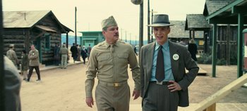 Movie still from “Oppenheimer” (2023), directed by Christopher Nolan – Two men walking down the street in suits and hats; Medium shot, Low angle