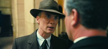 Movie still from “Oppenheimer” (2023), directed by Christopher Nolan – A man wearing a suit and hat talking to another man wearing a suit and hat; Close Up shot, Over the shoulder angle
