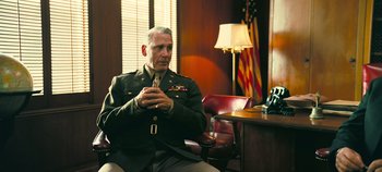 Movie still from “Oppenheimer” (2023), directed by Christopher Nolan – An older man in a military uniform sitting in a chair in front of a desk; Medium shot, Low angle