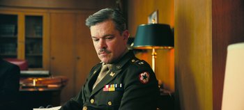 Movie still from “Oppenheimer” (2023), directed by Christopher Nolan – A man in a military uniform sitting in front of a lamp; Close Up shot, Low angle