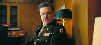 Movie still from “Oppenheimer” (2023), directed by Christopher Nolan – A man in a military uniform sitting in front of a lamp; Close Up shot, Low angle