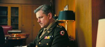 Movie still from “Oppenheimer” (2023), directed by Christopher Nolan – A man in a military uniform sitting in front of a lamp; Close Up shot, Low angle