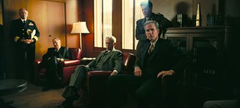 Movie still from “Oppenheimer” (2023), directed by Christopher Nolan – A group of men in suits sitting in a room; Wide shot, Low angle