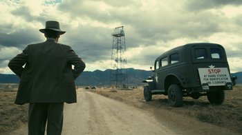 Movie still from “Oppenheimer” (2023), directed by Christopher Nolan – A man standing on a dirt road next to an old truck; Wide shot, Low angle