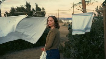 Movie still from “Oppenheimer” (2023), directed by Christopher Nolan – A woman standing in front of a clothesline holding a bag; Medium shot, Low angle