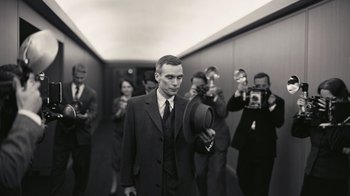 Movie still from “Oppenheimer” (2023), directed by Christopher Nolan – A group of people taking pictures of a man in a suit and tie; Medium shot, Low angle