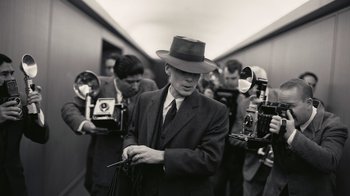Movie still from “Oppenheimer” (2023), directed by Christopher Nolan – A black and white photo of a man in a suit and a hat; Medium shot, Over the shoulder angle