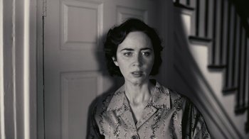Movie still from “Oppenheimer” (2023), directed by Christopher Nolan – Black and white photograph of a young woman in front of a door; Close Up shot, Low angle