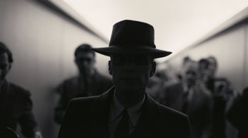 Movie still from “Oppenheimer” (2023), directed by Christopher Nolan – A black and white photo of a man in a suit and a hat; Close Up shot, Low angle