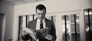 Movie still from “Oppenheimer” (2023), directed by Christopher Nolan – A man in a suit and tie reading a magazine; Medium shot, Low angle