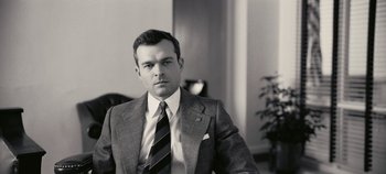 Movie still from “Oppenheimer” (2023), directed by Christopher Nolan – Black and white photograph of a man wearing a suit and tie; Close Up shot, Low angle
