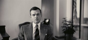 Movie still from “Oppenheimer” (2023), directed by Christopher Nolan – Black and white photograph of a man wearing a suit and tie; Close Up shot, Low angle