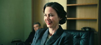 Movie still from “Oppenheimer” (2023), directed by Christopher Nolan – A woman in a suit smiling for the camera; Close Up shot, Over the shoulder angle