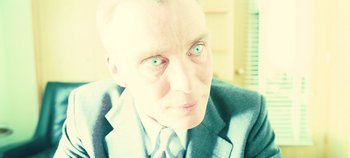 Movie still from “Oppenheimer” (2023), directed by Christopher Nolan – An older man in a suit and tie looking at the camera; Close Up shot, Low angle