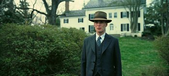 Movie still from “Oppenheimer” (2023), directed by Christopher Nolan – A man in a suit and hat standing in front of a house; Medium shot, Low angle