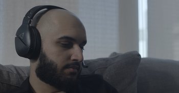 Movie still from “Outside” (2021), directed by Farahd Wallizada – A man with a headset on sitting on a couch; Close Up shot, Low angle