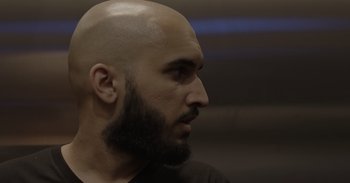 Movie still from “Outside” (2021), directed by Farahd Wallizada – A bald man with a beard looking to his left; Extreme Close Up shot, Low angle
