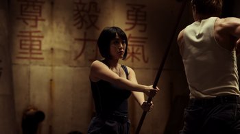 Movie still from “Pacific Rim” (2013), directed by Guillermo del Toro – A woman holding a wooden stick in front of a wall; Medium shot, Low angle