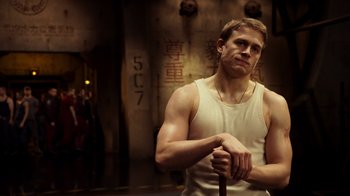 Movie still from “Pacific Rim” (2013), directed by Guillermo del Toro – A man holding a walking stick while wearing a tank top; Medium shot, Low angle