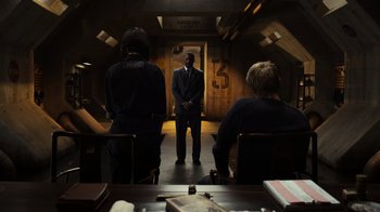 Movie still from “Pacific Rim” (2013), directed by Guillermo del Toro – A man in a suit standing in front of a group of people; Wide shot, Over the shoulder angle