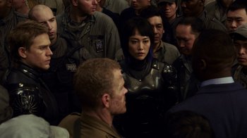 Movie still from “Pacific Rim” (2013), directed by Guillermo del Toro – A group of people standing around a man in a military uniform; Medium shot, Over the shoulder angle