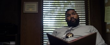 Movie still from “Palmer” (2021), directed by Fisher Stevens – A man sitting in a chair with a book; Medium shot, Low angle