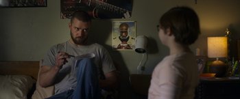 Movie still from “Palmer” (2021), directed by Fisher Stevens – A man sitting in front of a picture of a man; Medium shot, Over the shoulder angle