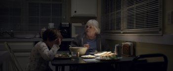 Movie still from “Palmer” (2021), directed by Fisher Stevens – An older woman sitting at a table with a bowl of food; Medium shot, Over the shoulder angle