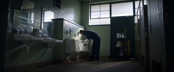 Movie still from “Palmer” (2021), directed by Fisher Stevens – A man in a bathroom washing his hands in a urinal; Wide shot, Low angle