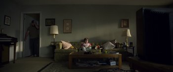 Movie still from “Palmer” (2021), directed by Fisher Stevens – A woman sitting on top of a couch in a living room; Wide shot, High angle