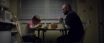 Movie still from “Palmer” (2021), directed by Fisher Stevens – A man and a child sitting at a table; Medium shot, Low angle