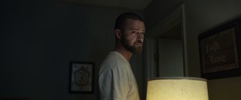 Movie still from “Palmer” (2021), directed by Fisher Stevens – A man standing next to a lamp in a dark room; Medium shot, Low angle