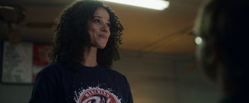 Movie still from “Palmer” (2021), directed by Fisher Stevens – A woman with curly black hair standing in front of a wall; Close Up shot, Over the shoulder angle