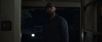 Movie still from “Palmer” (2021), directed by Fisher Stevens – A man wearing a hat and a dark jacket; Medium shot, Over the shoulder angle