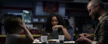 Movie still from “Palmer” (2021), directed by Fisher Stevens – A woman sitting at a table with food in front of her; Medium shot, Over the shoulder angle