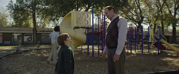 Movie still from “Palmer” (2021), directed by Fisher Stevens – A man and a boy standing in front of a playground; Medium shot, Over the shoulder angle