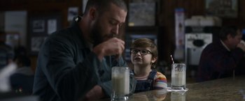 Movie still from “Palmer” (2021), directed by Fisher Stevens – A man and a child sitting in front of a glass of milk; Medium shot, Over the shoulder angle