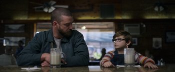 Movie still from “Palmer” (2021), directed by Fisher Stevens – A man sitting at a table next to a child; Medium shot, Over the shoulder angle