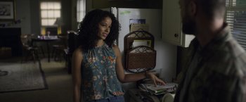 Movie still from “Palmer” (2021), directed by Fisher Stevens – A woman standing in a kitchen next to a stack of papers; Medium shot, Over the shoulder angle