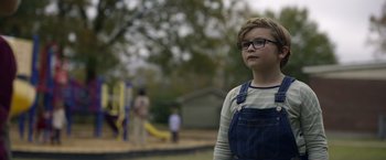 Movie still from “Palmer” (2021), directed by Fisher Stevens – A young boy wearing glasses standing in front of a playground; Close Up shot, Over the shoulder angle