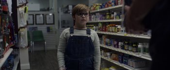 Movie still from “Palmer” (2021), directed by Fisher Stevens – A young boy wearing a pair of overalls in a grocery store; Medium shot, Low angle