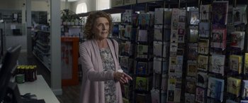 Movie still from “Palmer” (2021), directed by Fisher Stevens – An older woman is standing in front of a wall of greeting cards; Medium shot, Over the shoulder angle