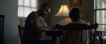 Movie still from “Palmer” (2021), directed by Fisher Stevens – A man sitting at a table writing on a piece of paper; Medium shot, Low angle
