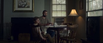 Movie still from “Palmer” (2021), directed by Fisher Stevens – A man and a boy sitting at a dining room table; Medium shot, Low angle