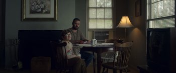 Movie still from “Palmer” (2021), directed by Fisher Stevens – A man and a boy sitting at a dining room table; Medium shot, Low angle