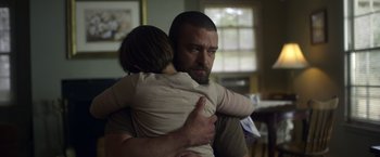 Movie still from “Palmer” (2021), directed by Fisher Stevens – A man holding a child in his arms in a living room; Medium shot, Over the shoulder angle