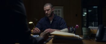 Movie still from “Palmer” (2021), directed by Fisher Stevens – A man sitting at a table writing on a piece of paper; Medium shot, Over the shoulder angle